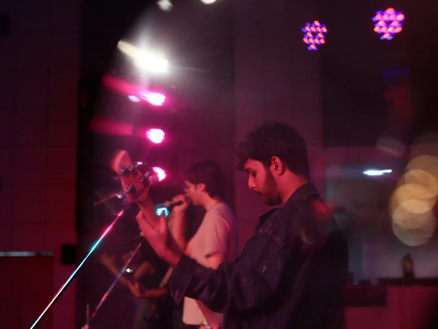 Bassist in magenta stage light with a vocalist behind
