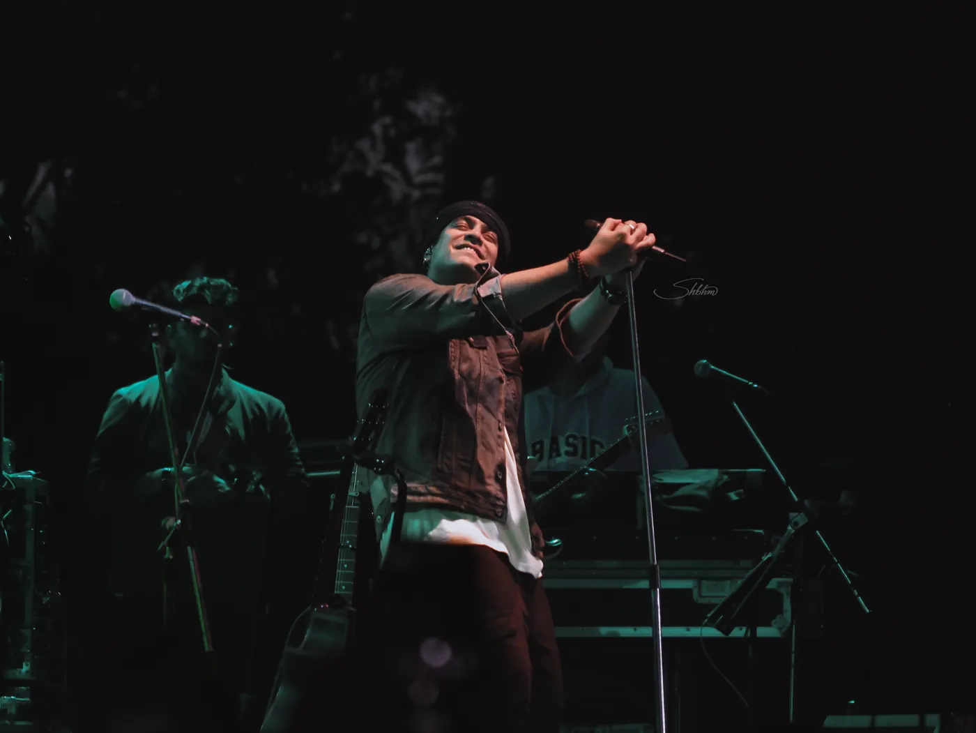 Singer gripping a microphone stand under green stage light